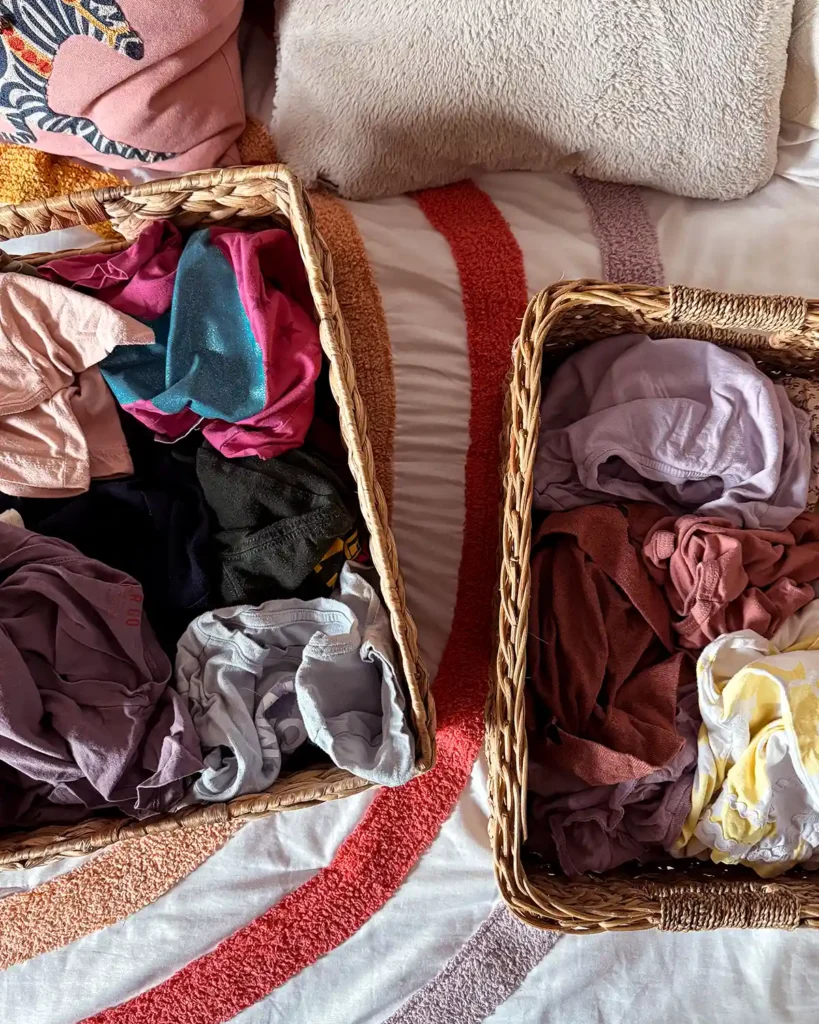Starting the declutter process by sorting kids clothes into piles in baskets before deciding what stays and goes