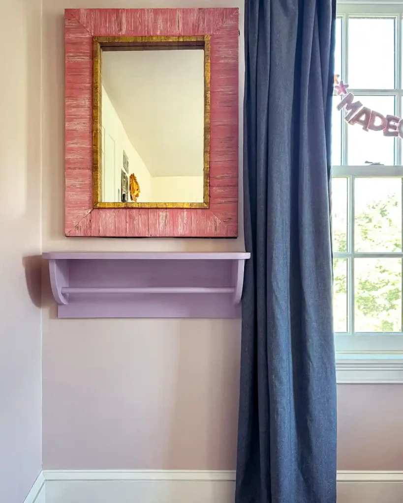 A purple painted wall-mounted DIY clothes rack in a girls' pink bedroom with a pink framed mirror hanging above it