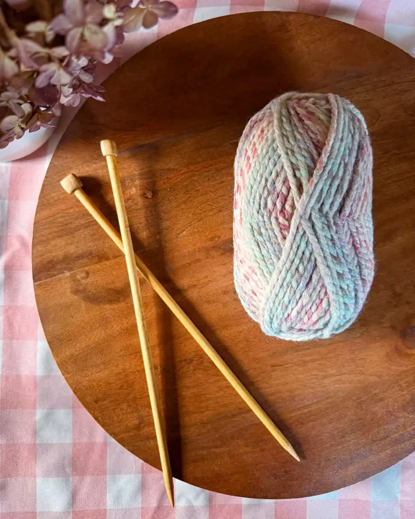 A pair of wooden knitting needles and a skein of yarn sitting on a wooden tray ready to start a new project