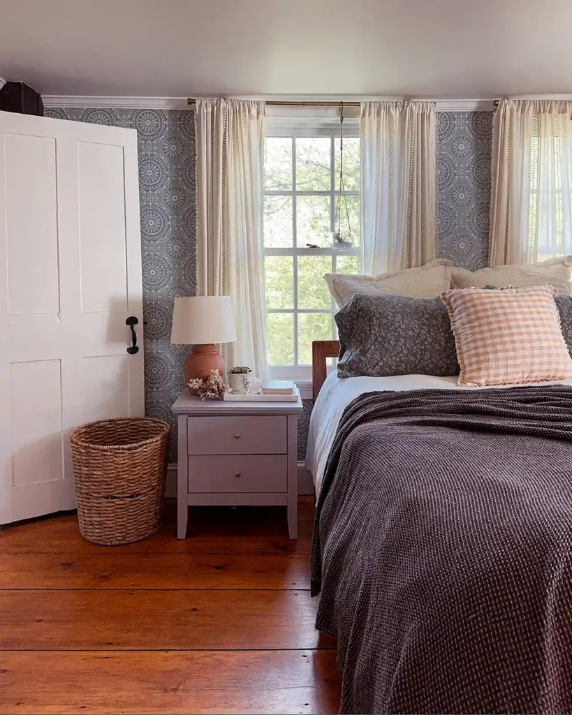 A bed layered with flannel sheets, duvet with a white linen cover, dark brown textured coverlet, and a golden yellow linen pillow for the perfect layered bedding for fall; bed in front of a pair of windows and next to a nightstand