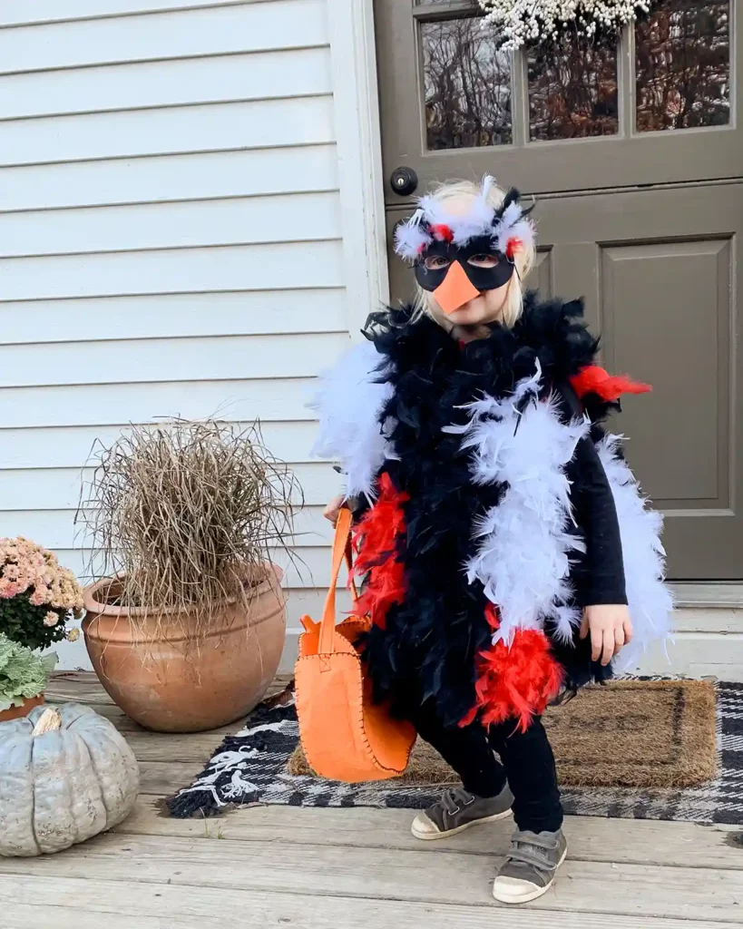 A child standing on the front porch wearing a DIY chicken Halloween costume made from feather boas