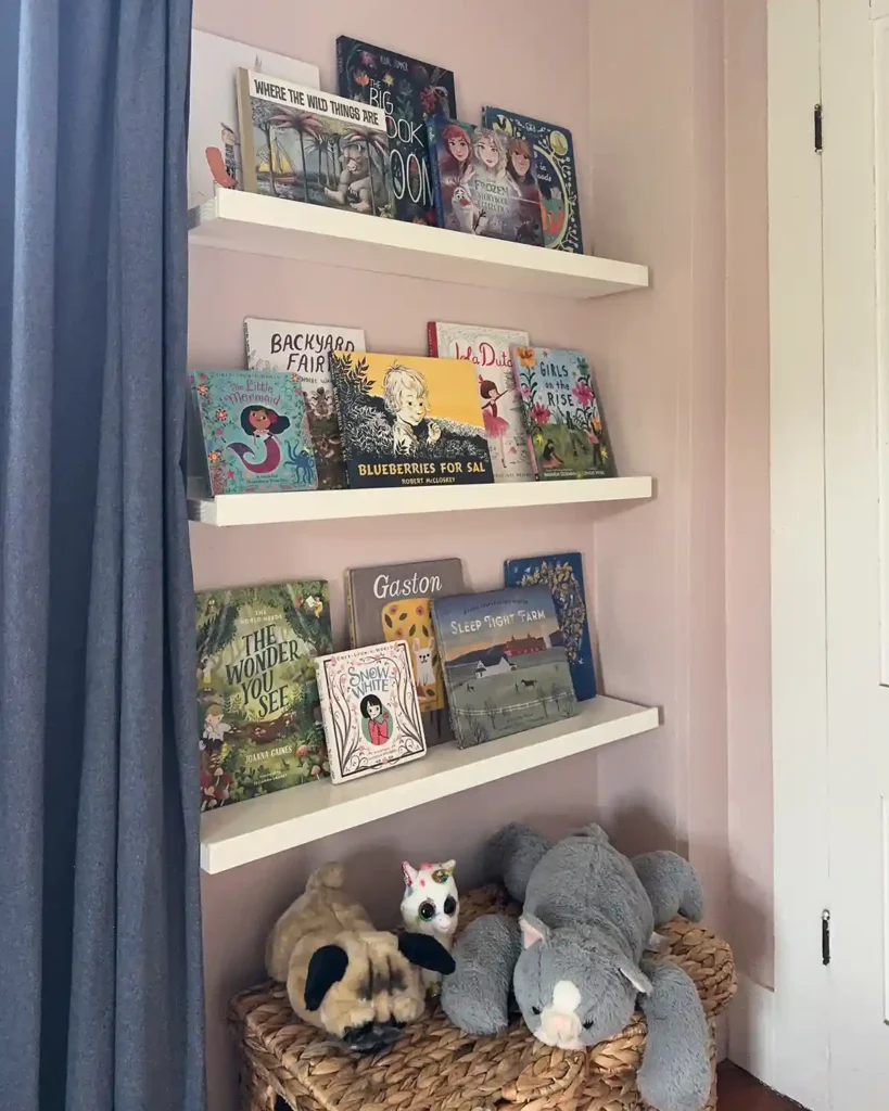Finished DIY ledge shelf for books in a little girls' room filled with picture books and board books; three shelves on the wall and a basket with stuffed animals underneath them