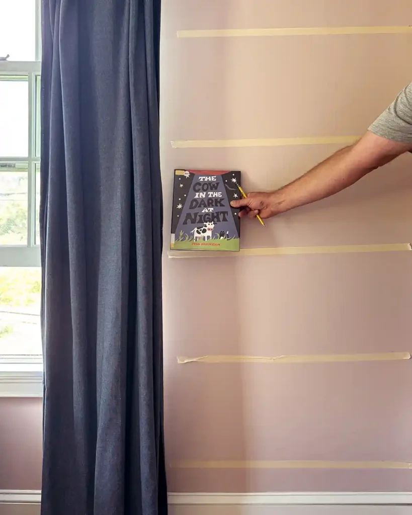 Using masking tape on the wall and holding up picture books to help us decide where to hang the ledge shelves