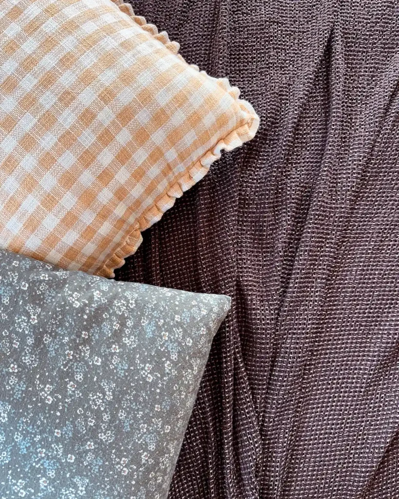 Mixing both patterns and textures with layered fall bedding with a golden yellow gingham patterned pillow in linen, moody blue and green flannel sheets, and a dark brown nubby coverlet that feels like silk