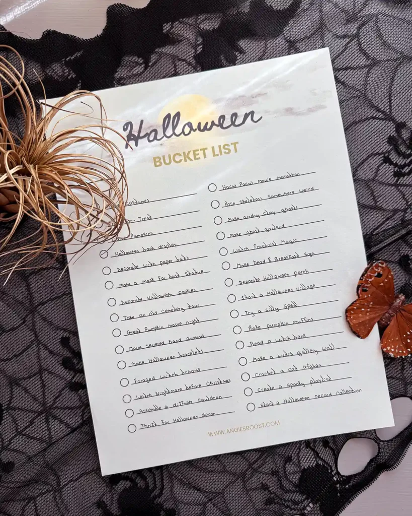 A filled out Halloween bucket list printable with all the activities a family wants to do during the Halloween season; paper is sitting on top of black lace with a dead plant and a fake moth sitting on it