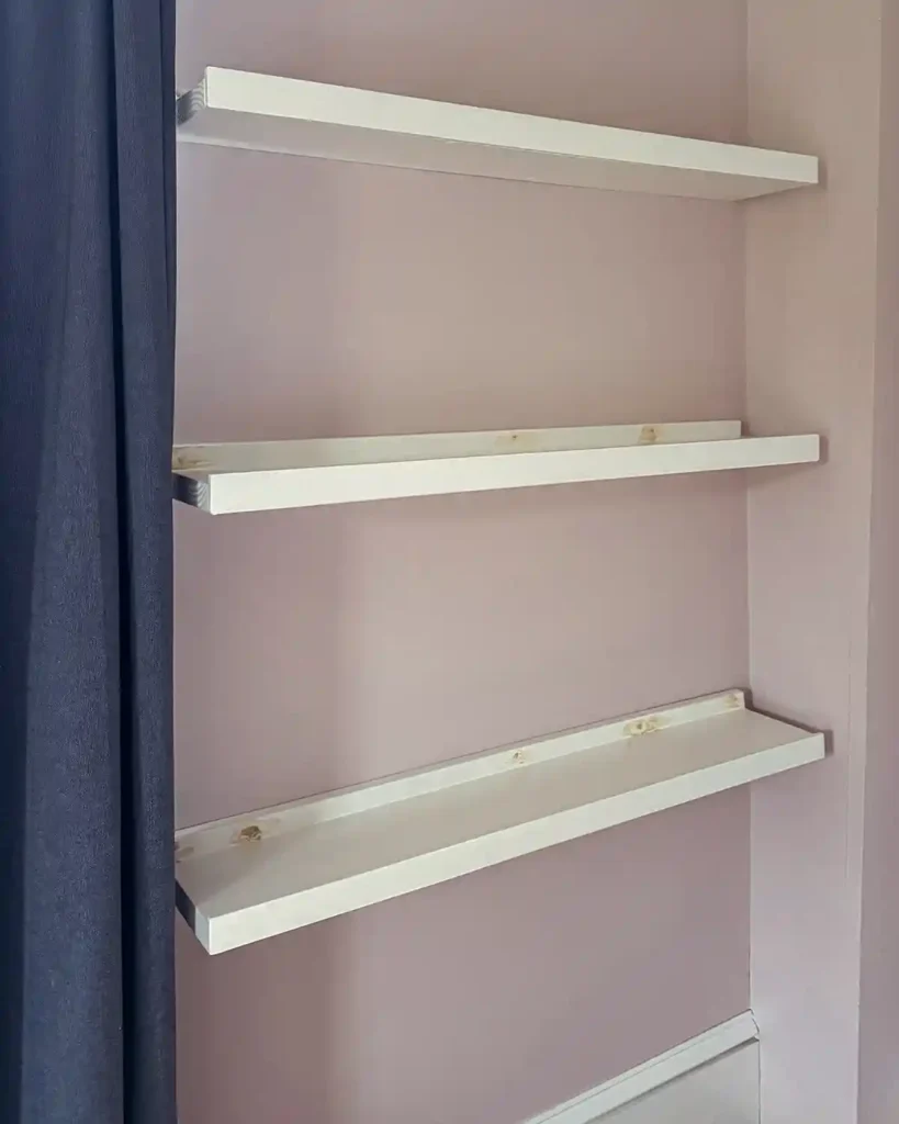Three white painted ledge shelves hung on the wall with the screw holes filled with natural wood colored wood filler