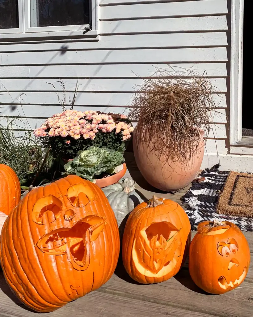 A trio of pumpkins carved during a pumpkin carving party with kids, all three pumpkins are sitting outside in a row on a deck with flowers behind them